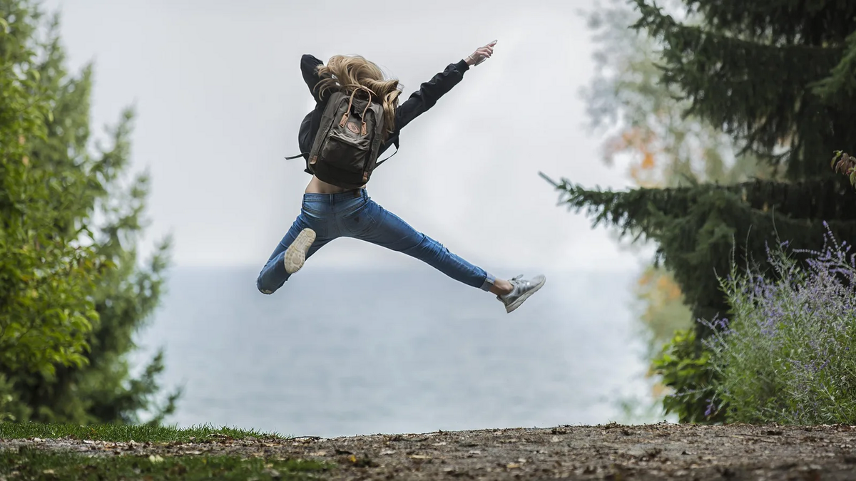 Symbolbild Freiwilligendienste. Wald mit Blick aufs Wasser. Eine Frau springt in die Luft. Foto: Pixabay.com | Pexels 